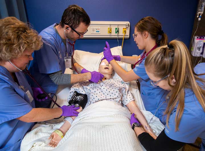 Four students in scrubs practicing on sim patient