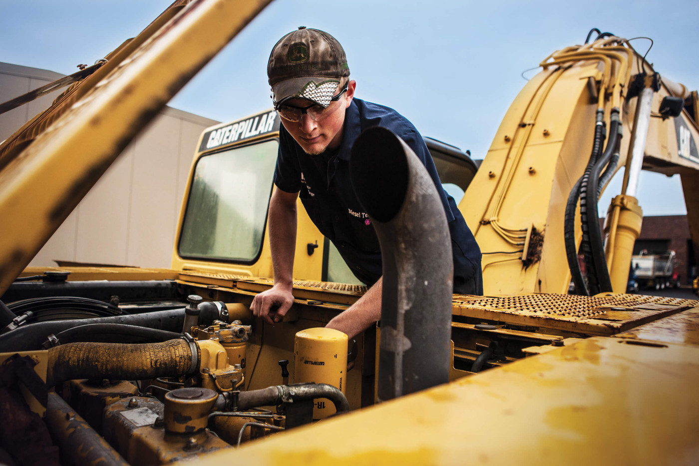 Diesel mechanic stands on top of a caterpillar, inspecting the diesel engine