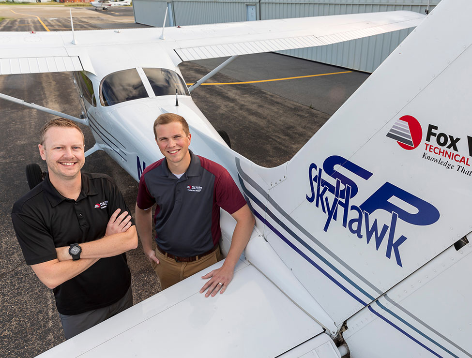 Two people smiling next to airplane