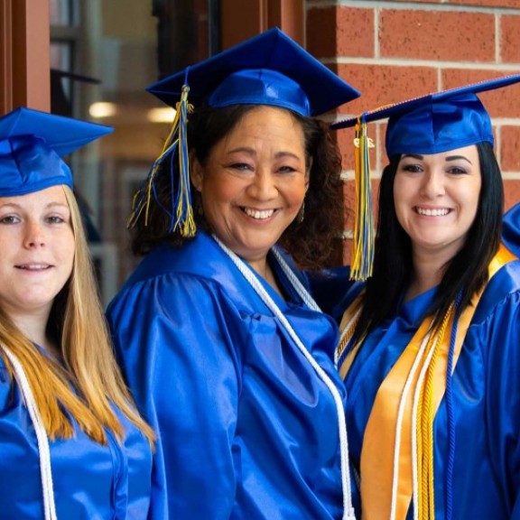 Five graduates in cap and gowns smiling together