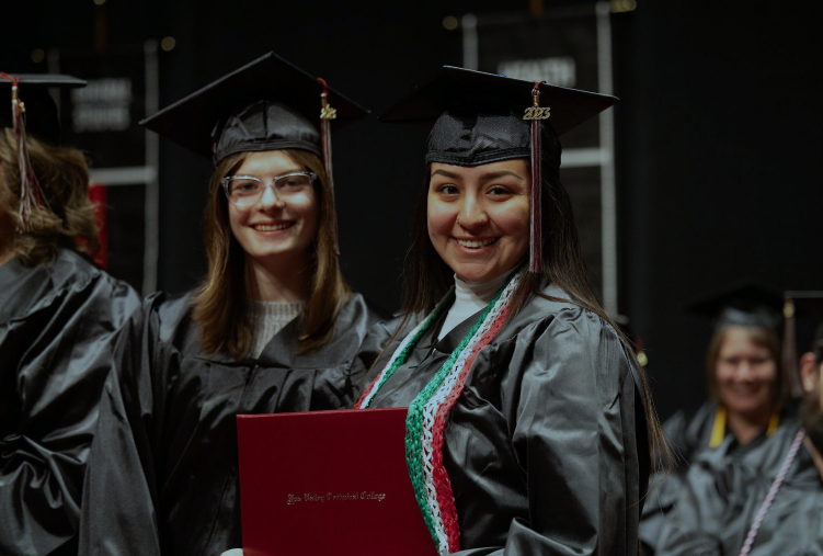 Graduates in black caps and gown smiling holding a diploma