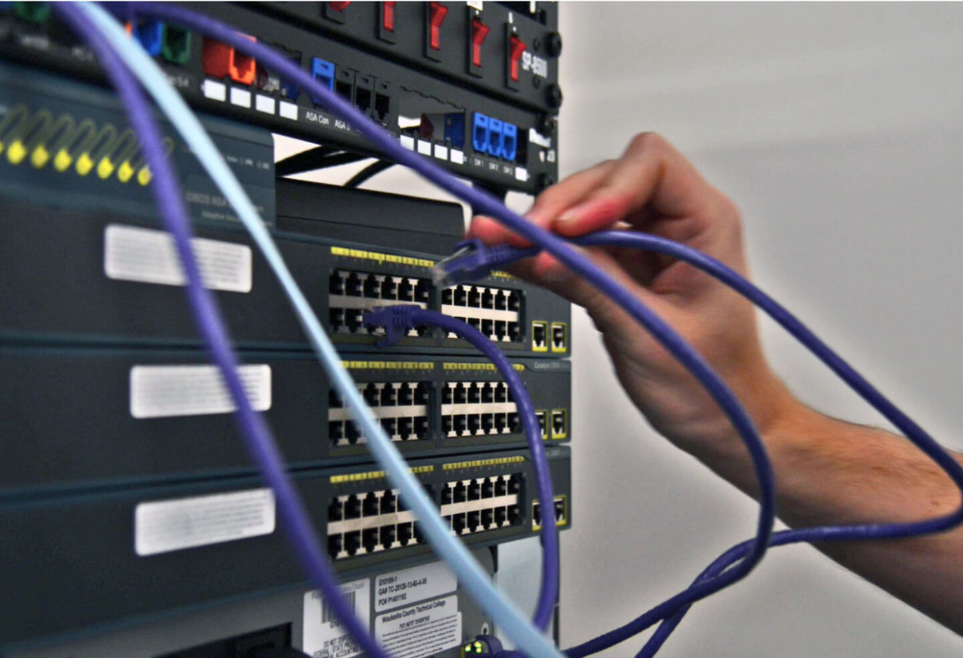 Image of a network server with someone plugging cables into it 
