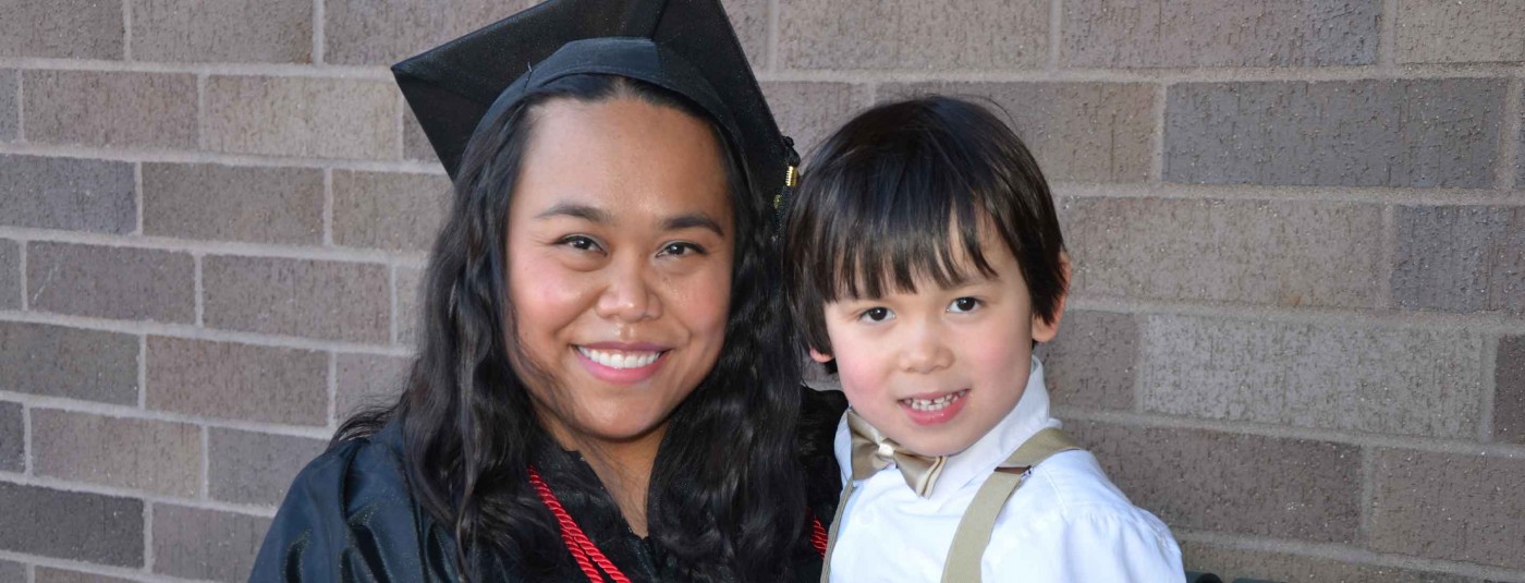 Graduate in cap and gown posing with child
