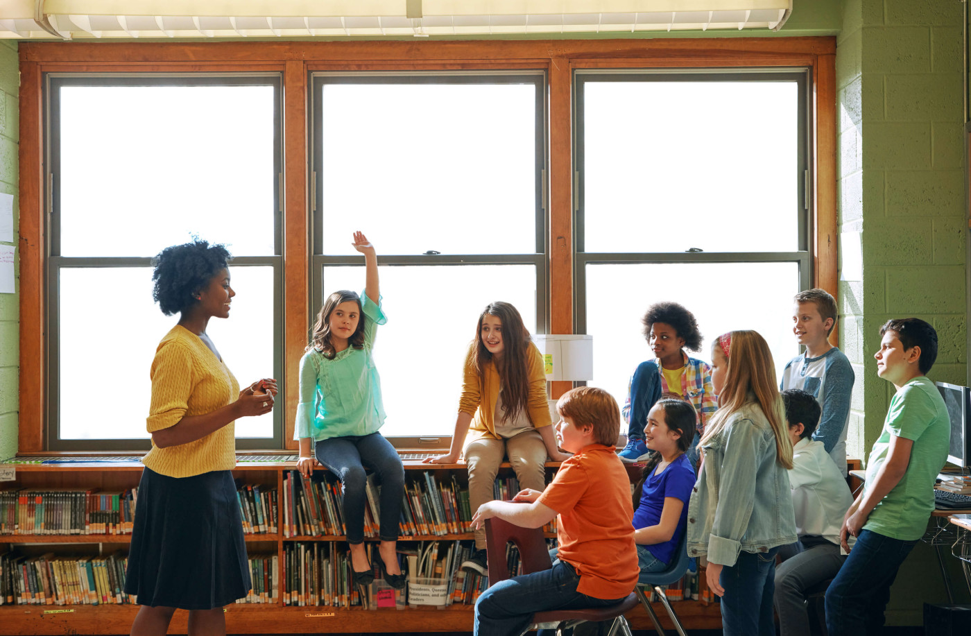 A young teacher apprentice leading a discussion with middle school students in a library