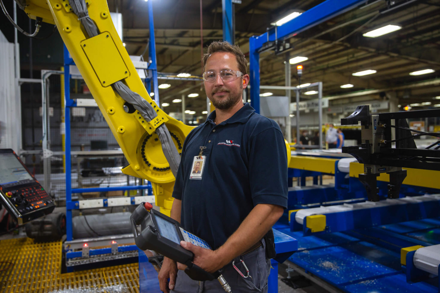 Man holding a tablet stands next to a programmable robot in a large facility