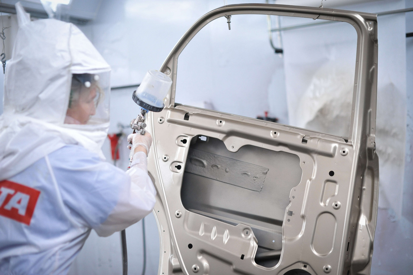 Technician in safety suit painting a car door