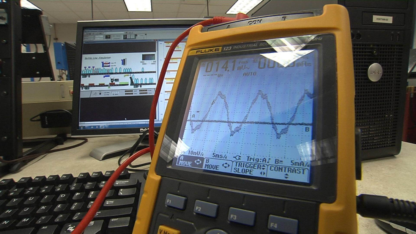 An industrial maintenance technician reading a handheld gauge with electronic probes