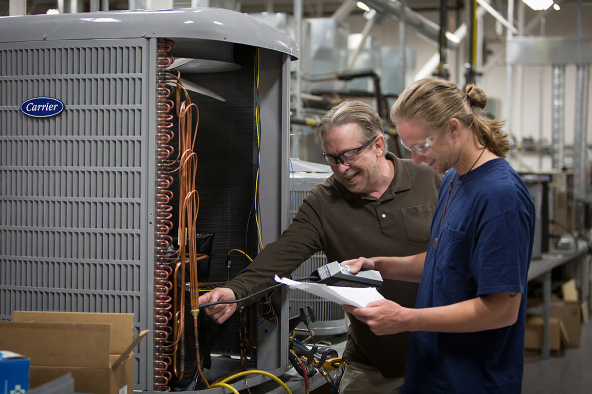 Student looking with an instructor at a commercial A/C unit in a large lab.