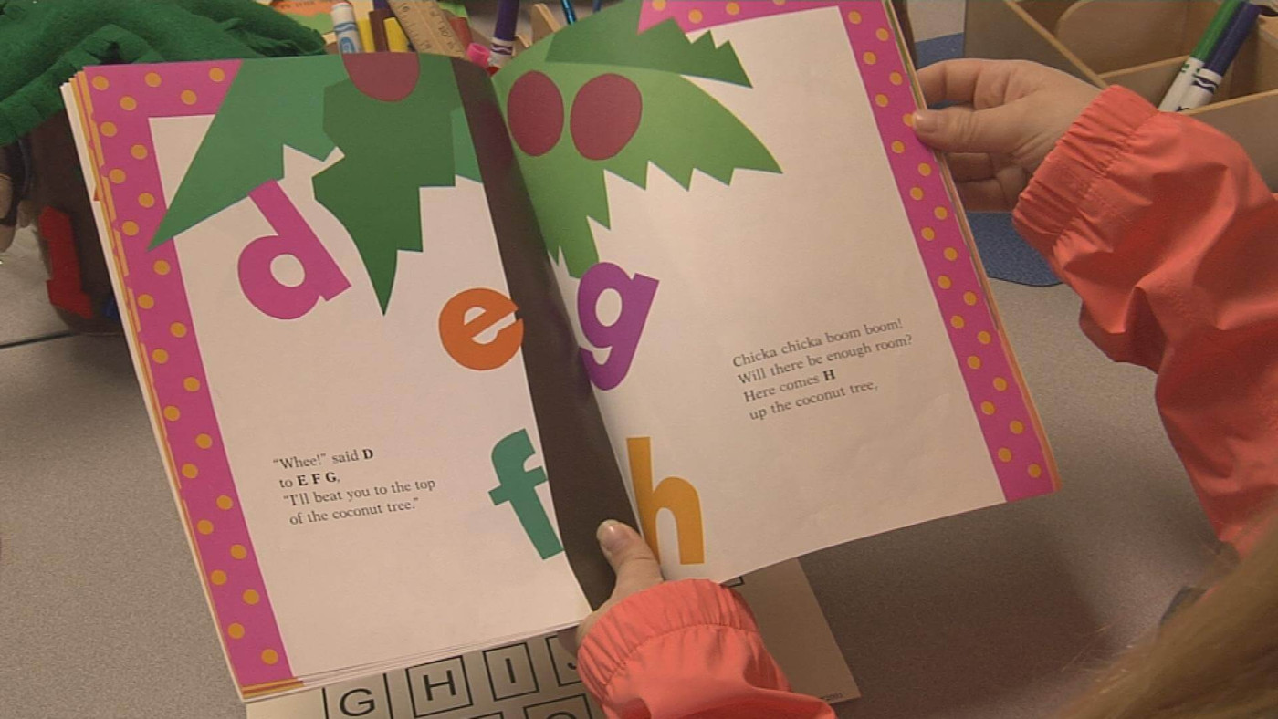 An educational Assistant helps a child sound out the words in a book