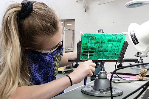 young woman with safety glasses on working on a motherboard from a biomedical equipment piece